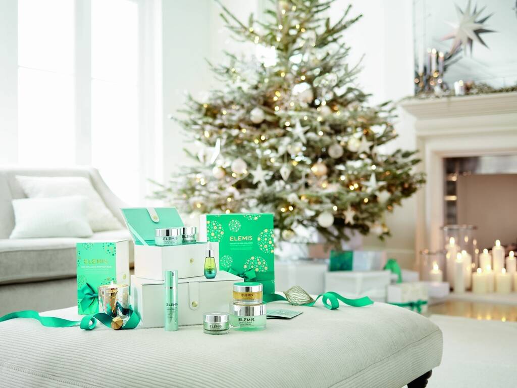 A stock image of a Christmas tree surrounded with Elemis skincare products, candles and white furniture