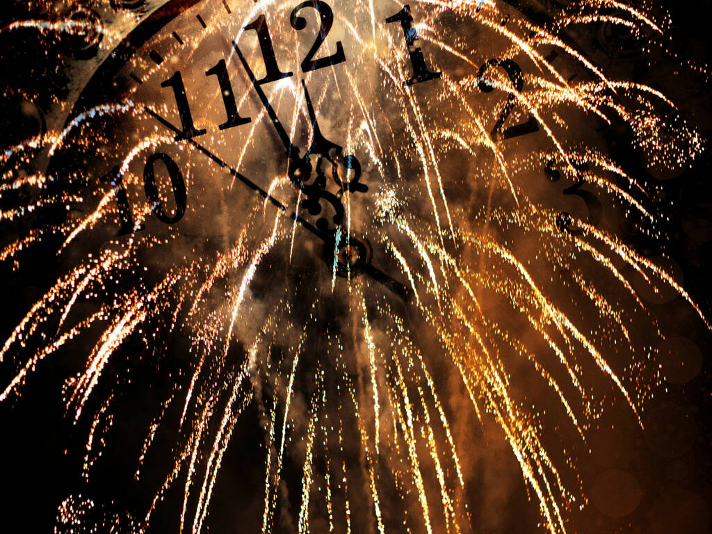 Fireworks in front of a clock about to strike for new years eve