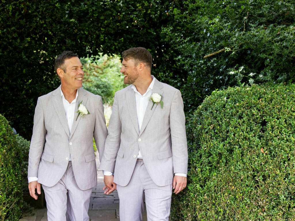 Grooms walk hand in hand through the vibrant gardens on their wedding day