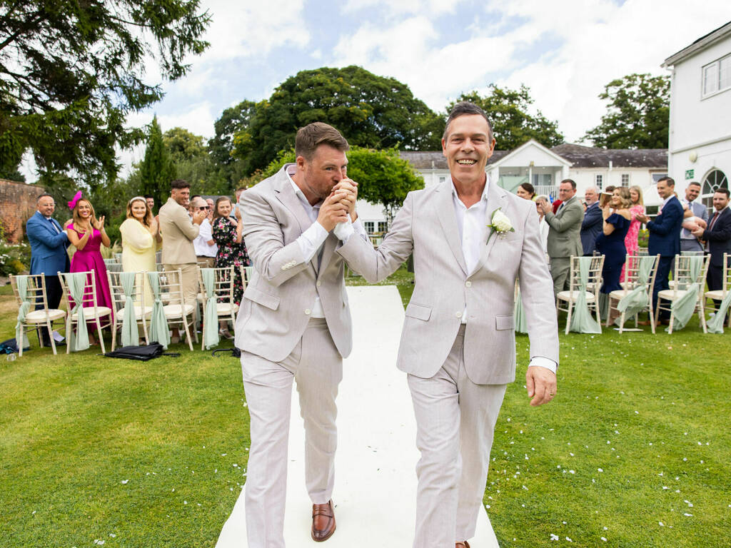 Grooms walk hand in hand after exchanging their vows at stunning outdoor wedding ceremony